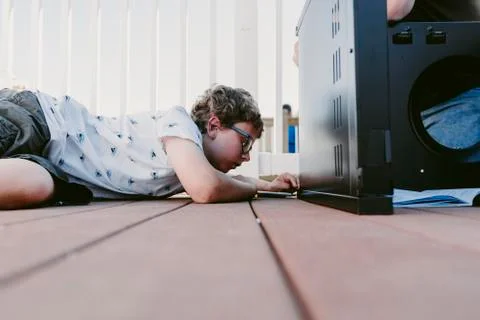 Surface level of boy using screw driver while making metallic cabinet on porch Foto stock