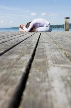 Surface level side view of mature woman sitting on pier bending over touching Stock Photos