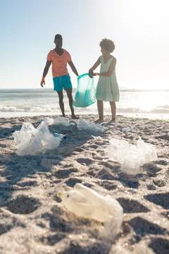 Surface level view of garbage on sand with african american couple collecting Stock Photos