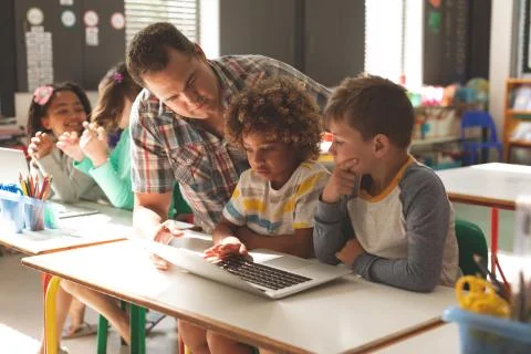 Surface level view of a teacher teaching how to use a laptop to his pupils Stock Photos