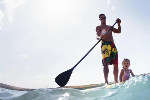 Surface level view of young man and toddler daughter standup paddleboarding Stock Photos
