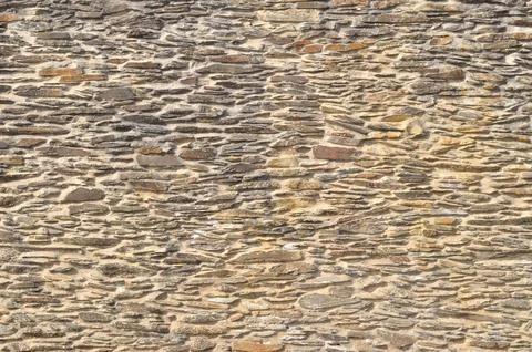 Surface texture of a wall built with small irregular beige stones Stock Photos