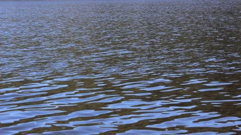 Surface of water with ripples - dark with reflections of blue sky Stock Photos