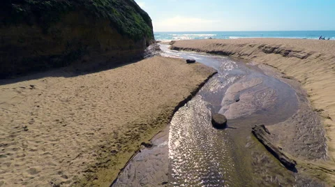 Surfer on beach as camera goes over small creek blue pacific ocean Stock Footage 62472267