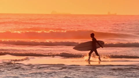 Surfer boy with his surfboard walking along the beach at sunset Stock Footage 138042161