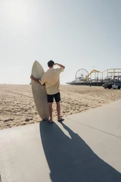 Surfer Casting Long Shadow On Pavement Toward Amusement Pier, Caucasian Male Stock-Fotos