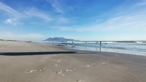 A surfer casting a long shadow walks down the beach before a session Stock Footage 133199367