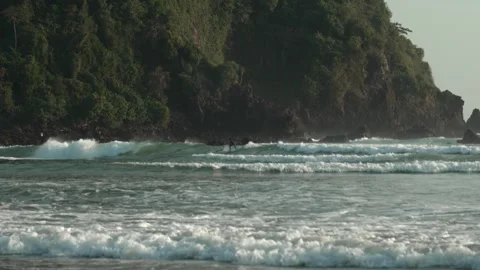 Surfer Catching Small Waves with Lush Island Backdrop at Pantai Pulau Merah Stock Footage 335379657