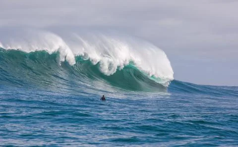 Surfer dwarfed by giant waves breaking off the coast of South Africa Stock Photos
