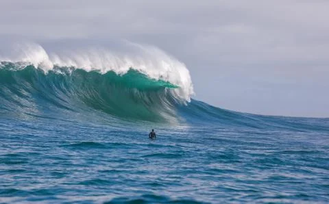 Surfer dwarfed by giant waves breaking off the coast of South Africa Stock Photos
