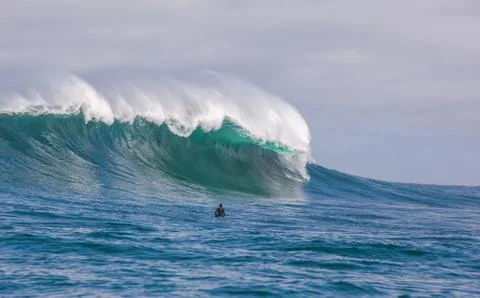 Surfer dwarfed by giant waves breaking off the coast of South Africa Stock Photos