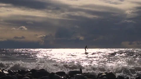 A surfer in the evening sun is trying to ride a wave with a paddle Stock Footage 169809534