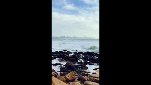 A surfer glides along the waves, against the backdrop of the metropolis. ocean.  Stock Footage 283218384
