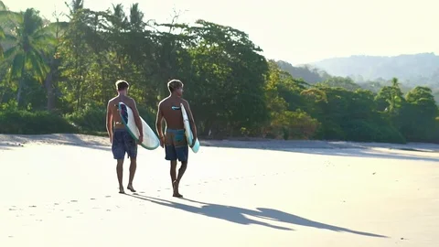 Surfer guys holding surf boards walking on beach at sunrise. Stock Footage 108564452
