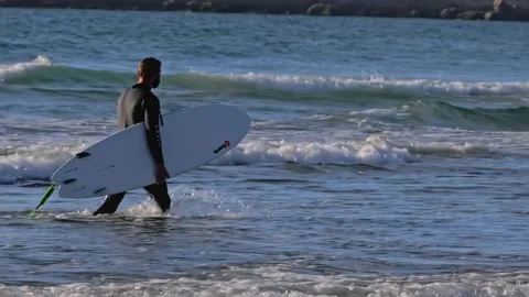 Surfer with his surfboard walking in ocean waves along Vídeo Stock 138025498
