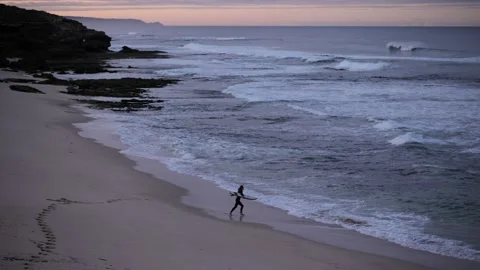 Surfer jumping into the ocean with a surfing board on the beach early morning  動画素材 196674828