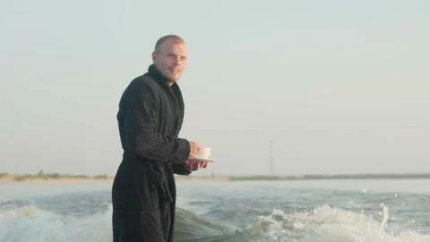 A surfer jumping on a wakeboard in a terry robe with a cup Stock Footage 160439249