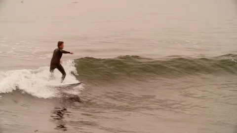Surfer at lighthouse point rides a disappointing wave on a cold foggy morning Stock Footage 93806474