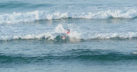 A surfer paddles on a surfboard through waves in the ocean. Stock Footage 243600911