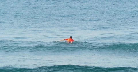 A surfer paddles on a surfboard through waves in the ocean. Stock Footage 244563875