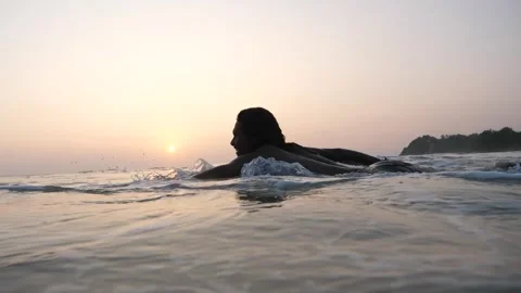 Surfer paddling past camera in sunset 스톡 동영상 274890024
