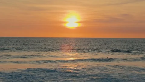 Surfer Paddling Through Gentle Waves Under Orange Sunset Sky Vídeo Stock 331189809