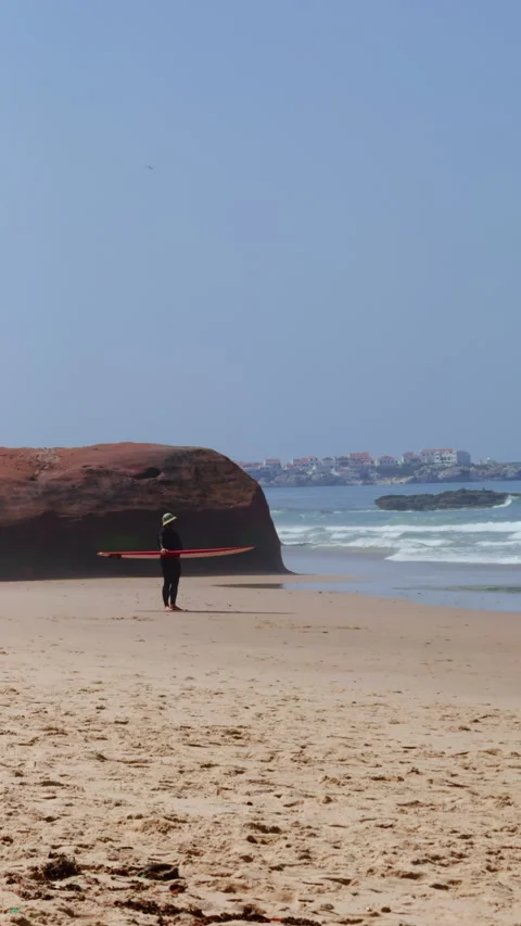 Surfer with Red Board by Rocky Cliff and Village Stock Footage 344947494