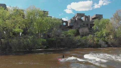 Surfer rides river wave near Habitat 67 building. Montreal, CA Stock Footage 314825341