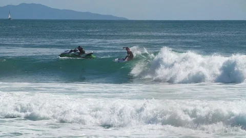 Surfer rides waves alongside jet skier on the ocean Stock Footage 93722798