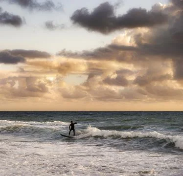 Surfer riding a wave during a dramatic sunset with colorful clouds over the.. Foto stock
