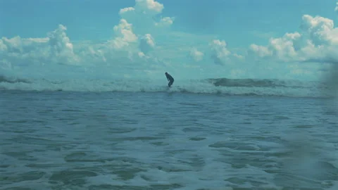 Surfer riding waves in ocean under bright blue sky with fluffy clouds. Stock Footage 285072941
