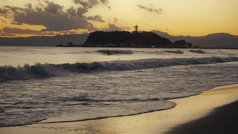 Surfer riding waves at sunset with enoshima island silhouette Stock Footage 324875869