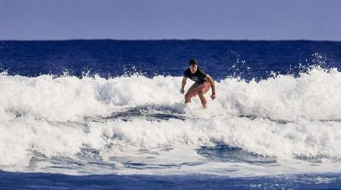 Surfer school. A young guy learning to stand on a surfboard. Surfer on the wa Stock Photos