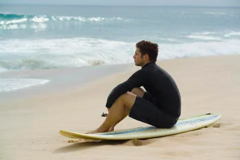 A surfer sitting on the beach Stock Photos