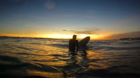 A surfer is sitting on a surfboard during sunset in the ocean Stock Footage 197932750