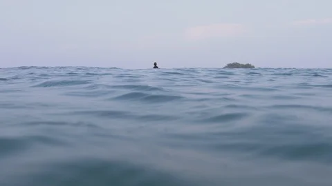 A surfer sitting on a surfboard waiting for waves / 4k 120fps slow motion / Shot Stockbeeldmateriaal 106855369