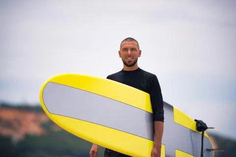 Surfer smiling, looking forward and holding surfboard on a sunny summer day. Stock Photos