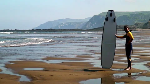 Surfer standing on beach holding surfboard with coastal view Stock Footage 336612495