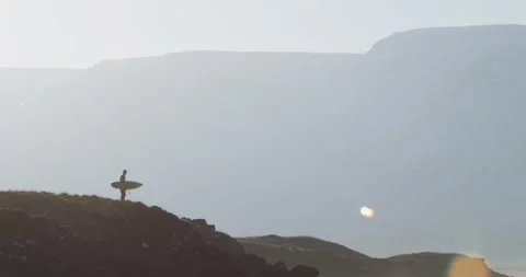 A surfer stands in front of snow covered mountains Video stock 234815941