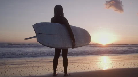 Surfer Stands Looking out at Ocean Holding Surfboard During Sunset Stock Footage 270393945