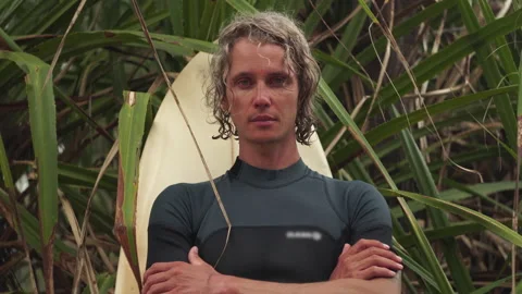 Surfer stands under palm tree with arms crossed on chest Stock Footage 163517093