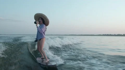 A surfer in a straw hat jumps on a wakeboard with champagne Stock Footage 160365927