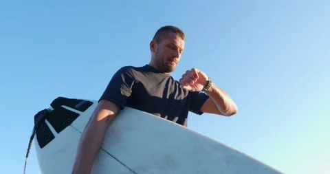 Surfer with surfboard checking time on hand watch. Stock Footage 220958701