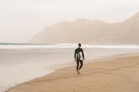 Surfer with surfboard in hands going through beautiful sand beach in Lanzarote Stock Photos