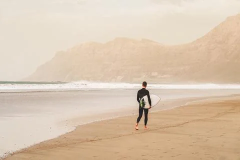 Surfer with surfboard in hands going through beautiful sand beach in Lanzarote Stock Photos