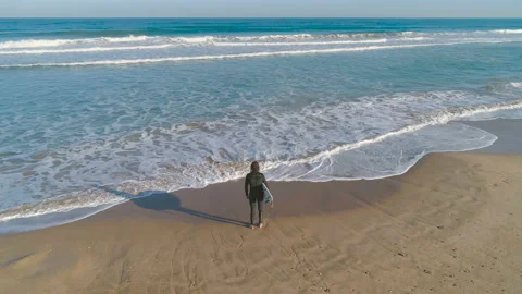 Surfer with surfboard standing on sand at the beach and looking on ocean waves Video stock 103270980
