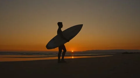 Surfer walking on the beach at sunset Stock Footage 308189877