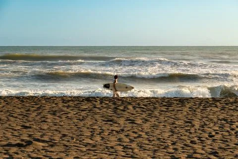 Surfer walking on beach with waves in the background Stock Photos