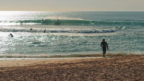 Surfer walking down the Atlantic Ocean beach with surfing board at sunset. Stock Footage 130628758