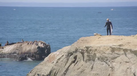 Surfer walking down a cliff at the beach to get into the water Stock Footage 64257068